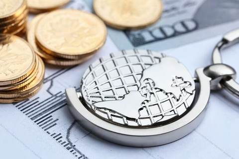 Moedas, cédula de cem dólares e globo metálico sobre gráficos financeiros impressos