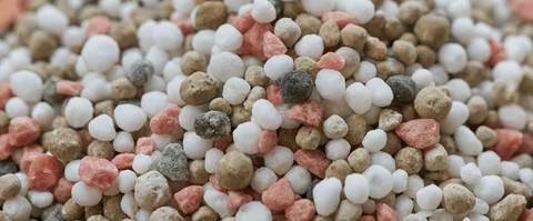 Close de grânulos de fertilizante mineral branco, rosa e marrom